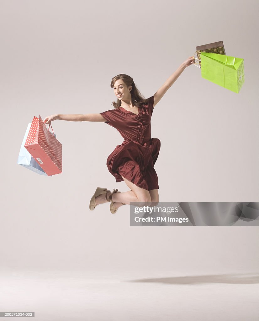 Young woman jumping in air with shopping bags, smiling