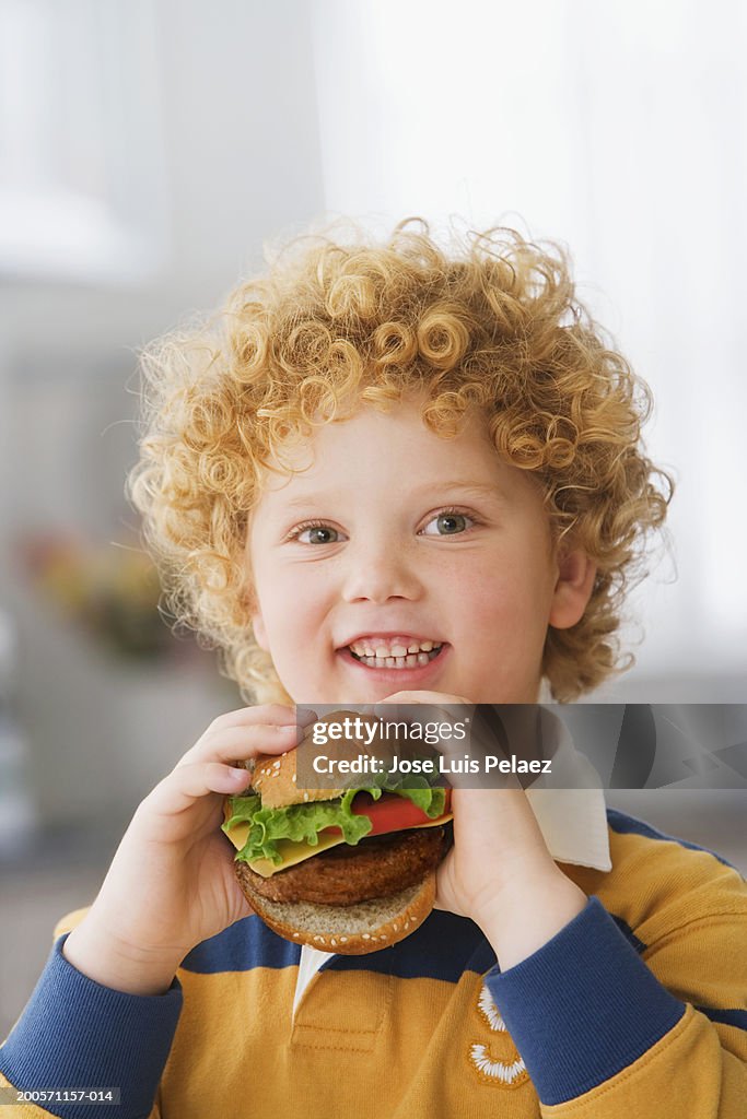 Boy (4-5) holding hamburger, smiling, close-up, portrait