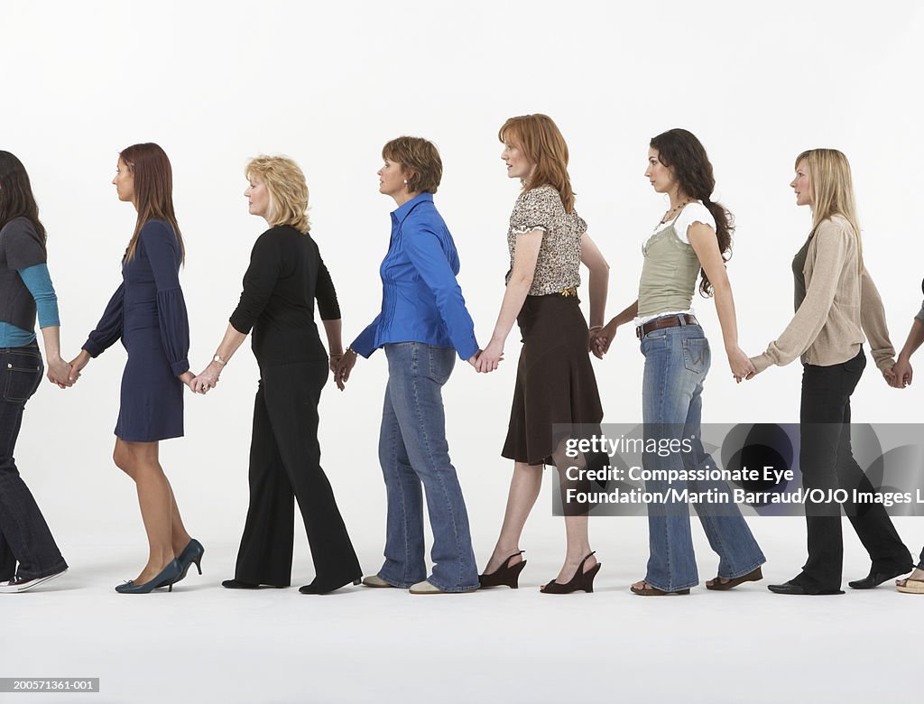 Group of women walking in row holding hands, side view
