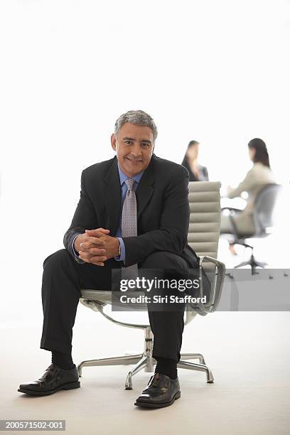 mature businessman sitting in office chair, women in background - woman straddling man stock pictures, royalty-free photos & images
