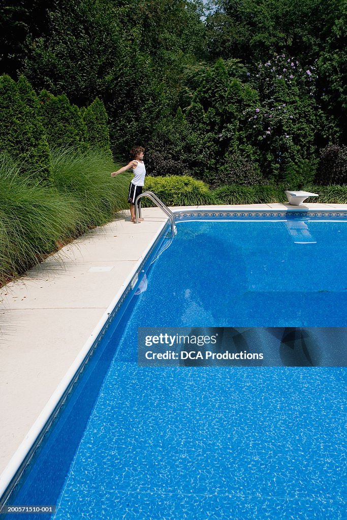 Boy (8-9) standing at poolside, side view