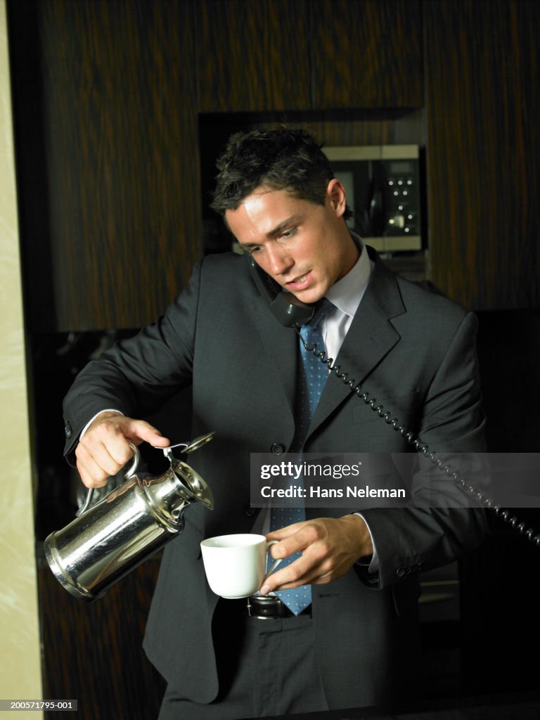 Businessman using phone while pouring coffee