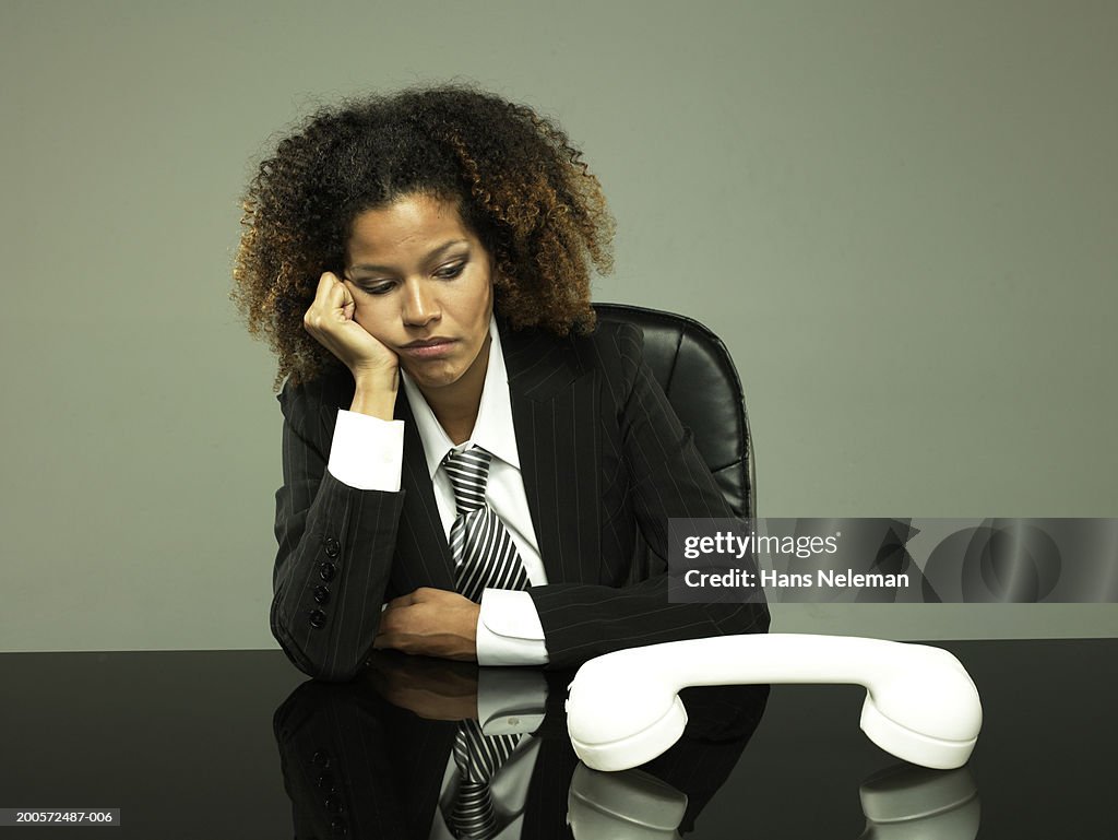 Young business woman sitting, oversized phone on desk