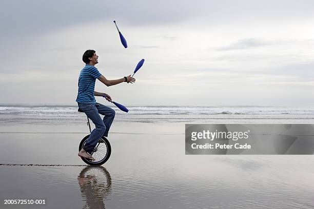 young man riding unicycle while juggling - eficacia fotografías e imágenes de stock