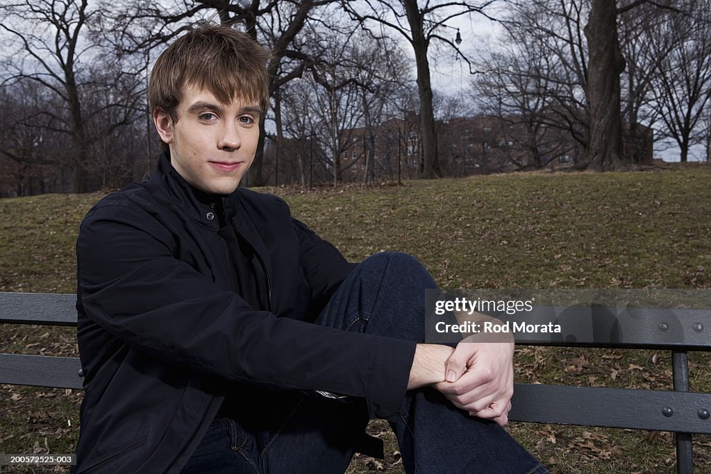 Young man sitting on bench in park, smiling