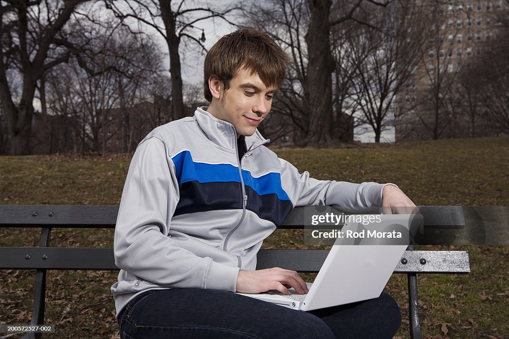 Young man using laptop on bench in park