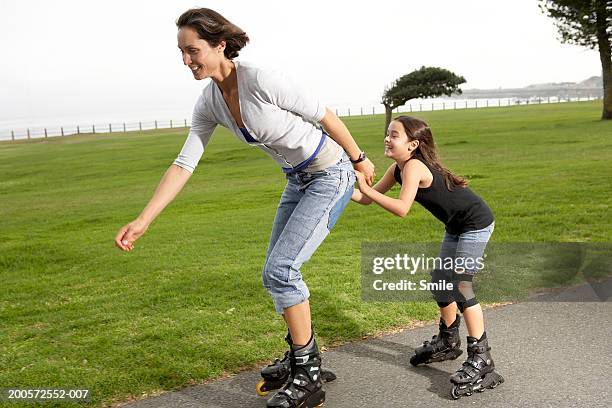 mother and daughter (8-10) rollerblading in park - smile woman child stock-fotos und bilder