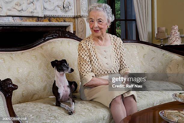 senior woman sitting on sofa with dog, smiling - etiquette stock-fotos und bilder