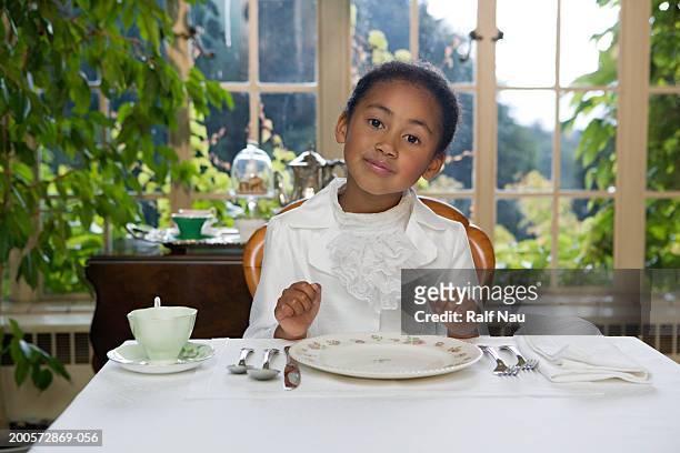 girl (5-7) sitting at table setting, smiling - reglas de sociedad fotografías e imágenes de stock