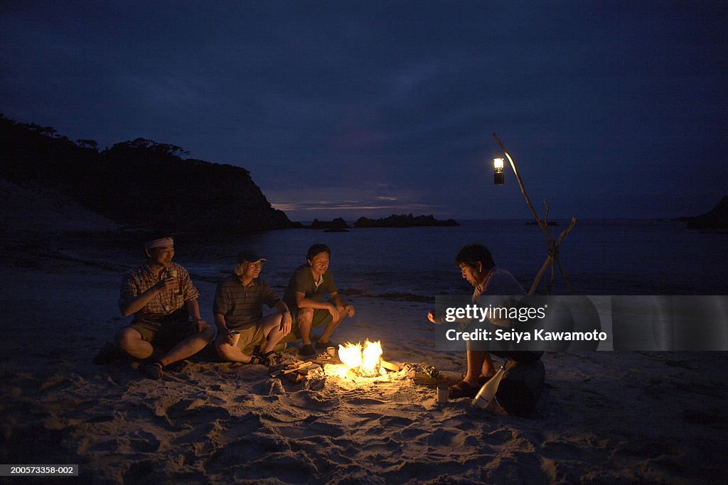 Friends sitting around campfire on beach at night