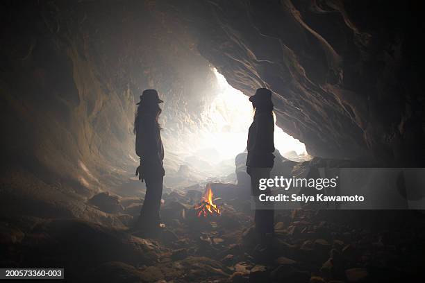 two women standing by fire in cave - cave fire stock pictures, royalty-free photos & images