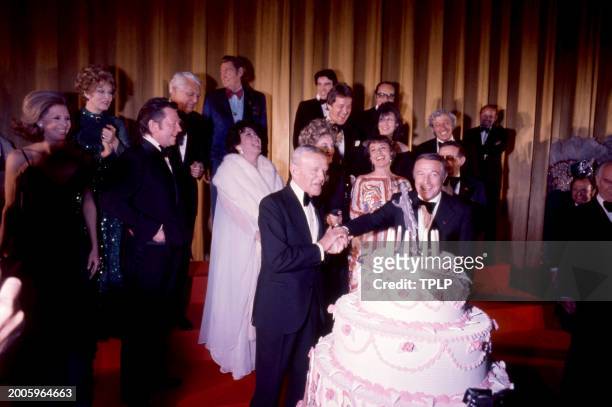 American actor and dancer Fred Astaire takes the hand of Gene Kelly celebrating Astaire's 77th birthday during a party at Ziegfield Theater following...
