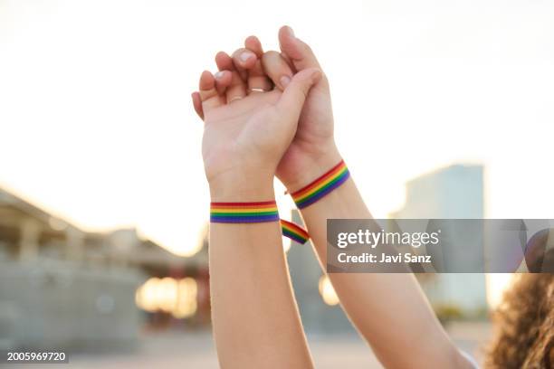 lesbisches verliebtes mädchenpaar, das mit regenbogenarmbändern händchen hält und die lgbt-pride-day-parade feiert. - armband stock-fotos und bilder