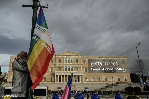 Person hangs a LGBTQ pride flag on a light pole outside the Greek Parliament during a gathering with fellow supporters of the LGBTQ community as...