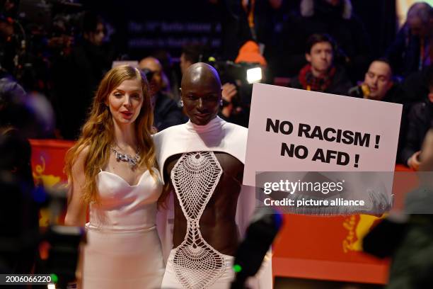 February 2024, Berlin: Papis Loveday stands on the opening night of the Berlinale with a protest sign "No Racism ! No AFD !" next to actress Pheline...