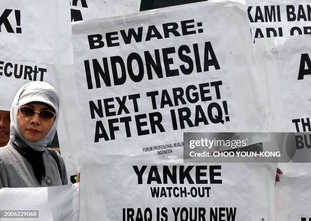 Muslim woman stand next to anti-US placards during a protest along a street in Jakarta, 19 August 2003. The protesters are against US, UK and...