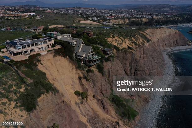 An aerial image shows homes along Scenic Drive standing on the edge of a cliff above the Pacific Ocean after a landslide following heavy rains in...