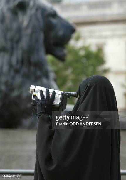 Woman in traditional moslem gowns videofilms her family under the watchfull eyes of the lions guarding the Nelson cloumn at Trafalgar square in...