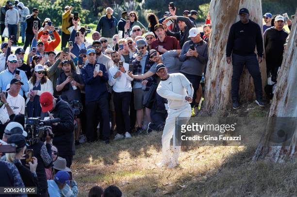 Tiger Woods hits out of the rough and between trees after shanking his fairway shot on the 18th hole during the first round of the Genesis...