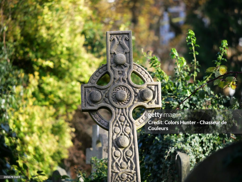 Close-up of an ancient Celtic stone cross decorated with dogs and snakes. Photograph taken at Brompton Cemetery in London, England, United Kingdom. Sunlight. Natural colors.