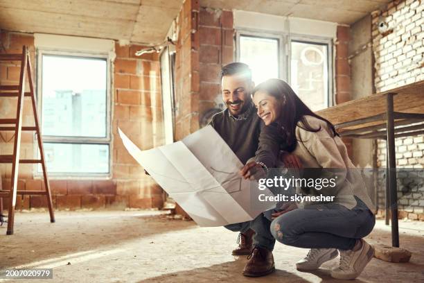 feliz pareja analizando planes en su apartamento renovador. - renovación del hogar fotografías e imágenes de stock