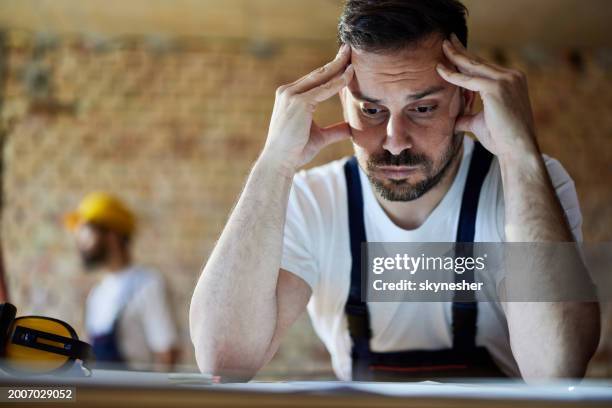 worried male worker analyzing blueprints at construction site. - policy maker stock pictures, royalty-free photos & images
