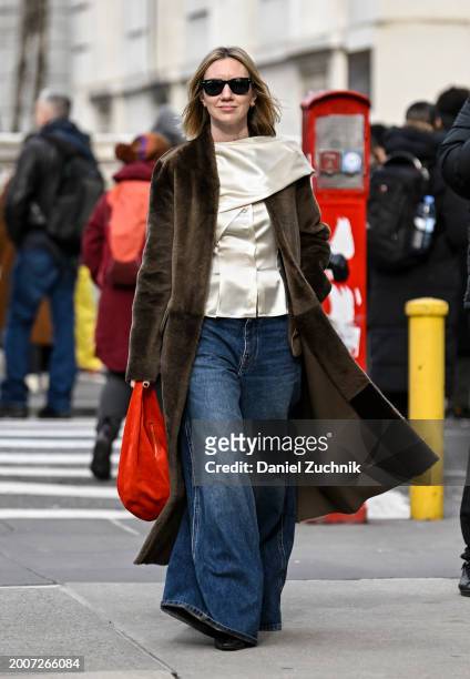 Lisa Aiken is seen wearing a brown coat, cream top, blue oversized jeans and red bag with black sunglasses outside the Coach show during NYFW F/W...