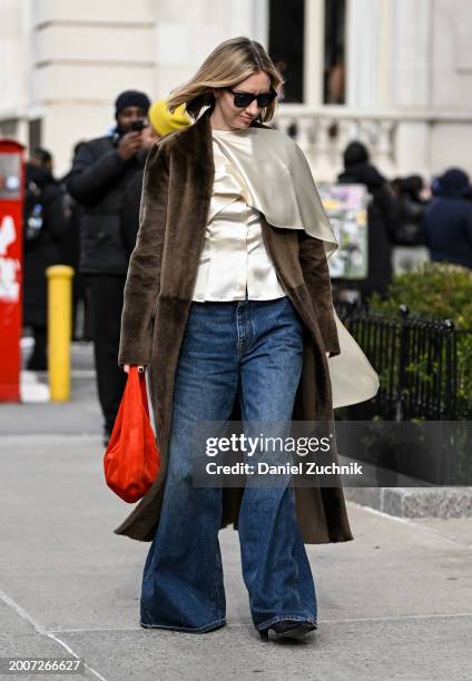 Lisa Aiken is seen wearing a brown coat, cream top, blue oversized jeans and red bag with black sunglasses outside the Coach show during NYFW F/W...