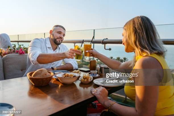 young couple cheering with drinks while having lunch in a restaurant in kuwait city - outdoor dining stock pictures, royalty-free photos & images