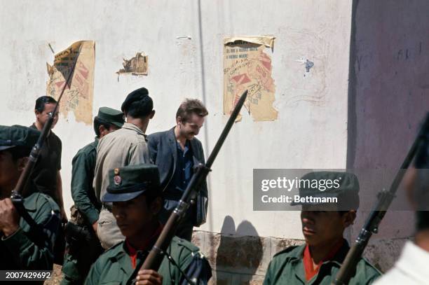French journalist Régis Debray walking behind armed guards as he leaves a courtroom in Camiri, Bolivia, where he is being tried on the charge of...