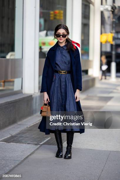 Kate Bartlett wears belted denim dress, navy coat, brown bag outside Carolina Herrera on February 12, 2024 in New York City.