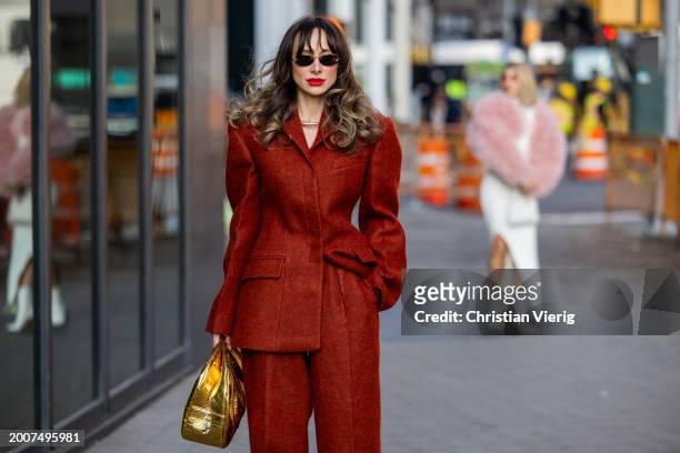 Guest wears red tailored blazer, wide leg pants, golden bag outside Carolina Herrera on February 12, 2024 in New York City.