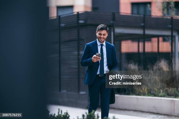 handsome smiling man in a suit on his way to work texting on his mobile phone - businessman stock pictures, royalty-free photos & images