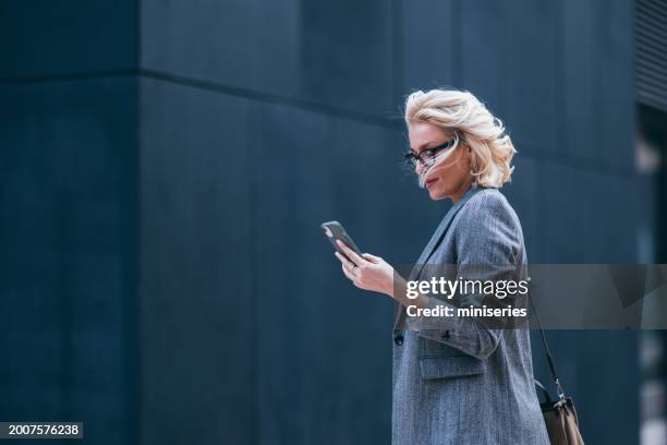 bella donna d'affari che cammina verso il suo ufficio di lavoro e legge un messaggio sul suo telefono cellulare - business woman foto e immagini stock