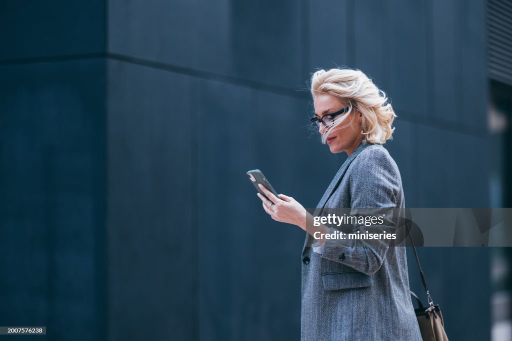 Beautiful Businesswoman Walking to Her Work Office and Reading a Message on Her Mobile Phone