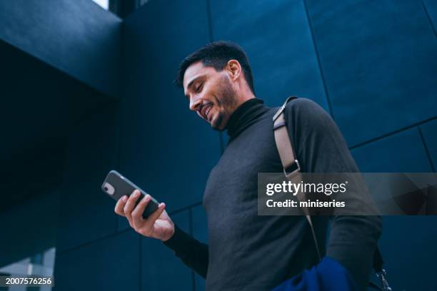 portrait of a handsome man waiting by the office building and reading a text message - homens imagens e fotografias de stock