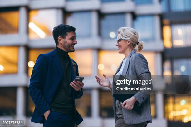 a handsome businessman and a beautiful businesswoman talking in the evening in front of the office building - mature man smiling 40 44 years blond hair stock pictures, royalty-free photos & images