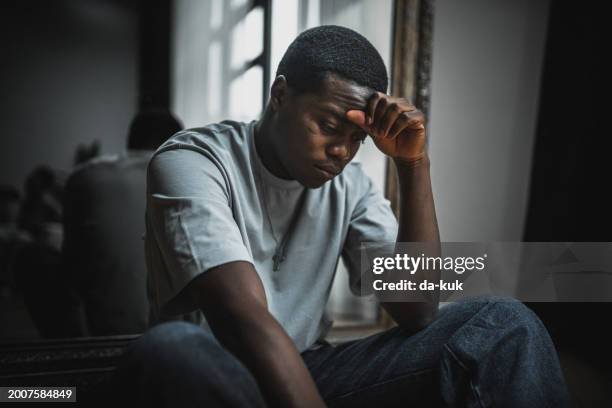 moment of depression, loneliness and emotional stress. young black man sits on the floor and looks very upset and stressed - histeria imagens e fotografias de stock