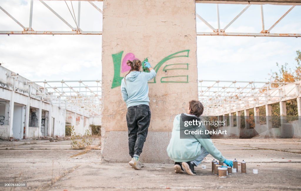 Rear view of two young street artists drawing graffiti on the wall of an abandoned building