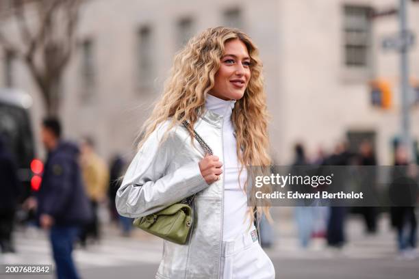 Emili Sindlev wears earrings, a silver shiny jacket, a white turtleneck top, a green leather Coach bag, white pants with printed green apples,...