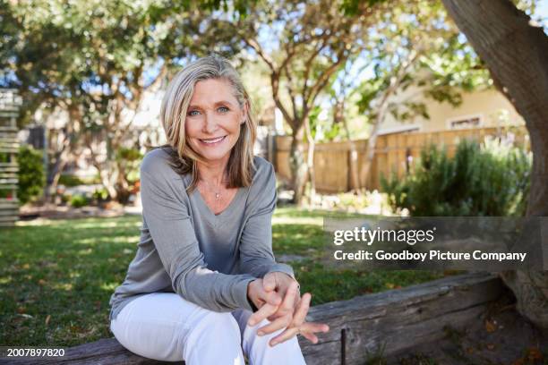 reife frau lächelt, während sie in ihrem sonnigen garten sitzt - einzelne frau über 40 stock-fotos und bilder