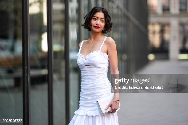Guest wears a low neck ruffled off-shoulder pleated gathered long dress, a bag, outside Carolina Herrera, during New York Fashion Week, on February...