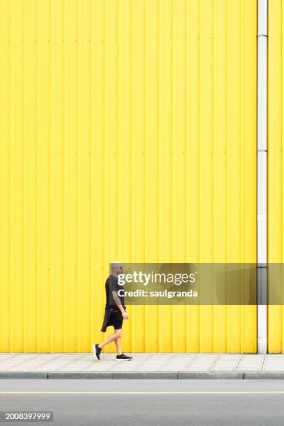 man in black walking on the street against a yellow wall - estilo de vida saludable stock-fotos und bilder