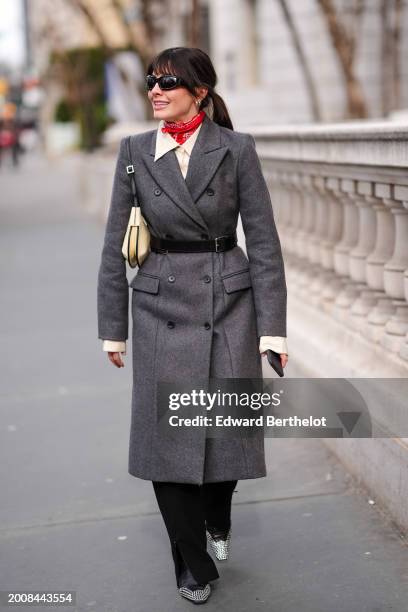 Guest wears sunglasses, earrings, a red scarf, a white shirt, a gray cotton trench long coat , a beige leather bag, a think belt, black pants ,...