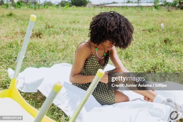 woman using mobile phone while sitting on field,tema,ghana - ghana phone stock pictures, royalty-free photos & images