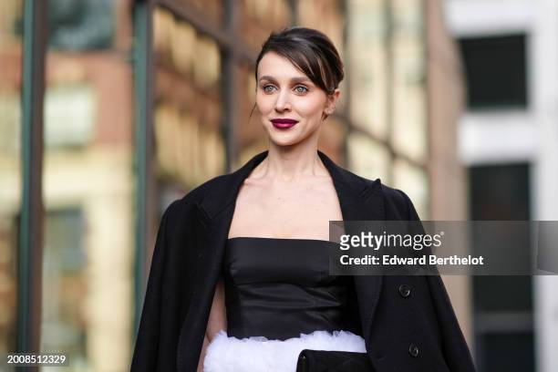 Mary Leest wears a black long coat, a black gathered off-shoulder top, a white fluffy mini skirt with floral details, tights, black and white pointed...