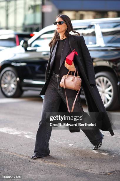 Guest wears sunglasses, a black long coat, a brown leather bag , a black top, black flared denim jeans pants black and white pointed shoes , outside...