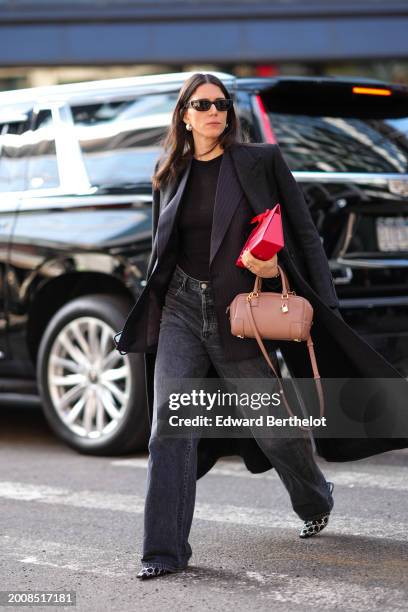 Guest wears sunglasses, a black long coat, a brown leather bag , a black top, black flared denim jeans pants black and white pointed shoes , outside...