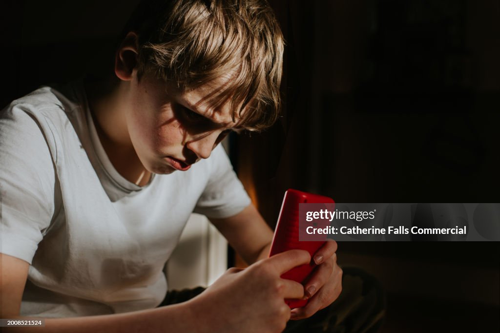 A young lad plays a retro, red, handheld games console