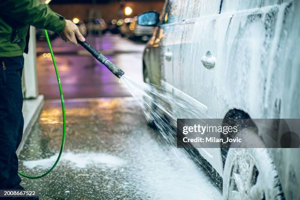 a man washes his car at a self-service car wash using a hose with pressurized water - splash wasser stockfoto's en -beelden